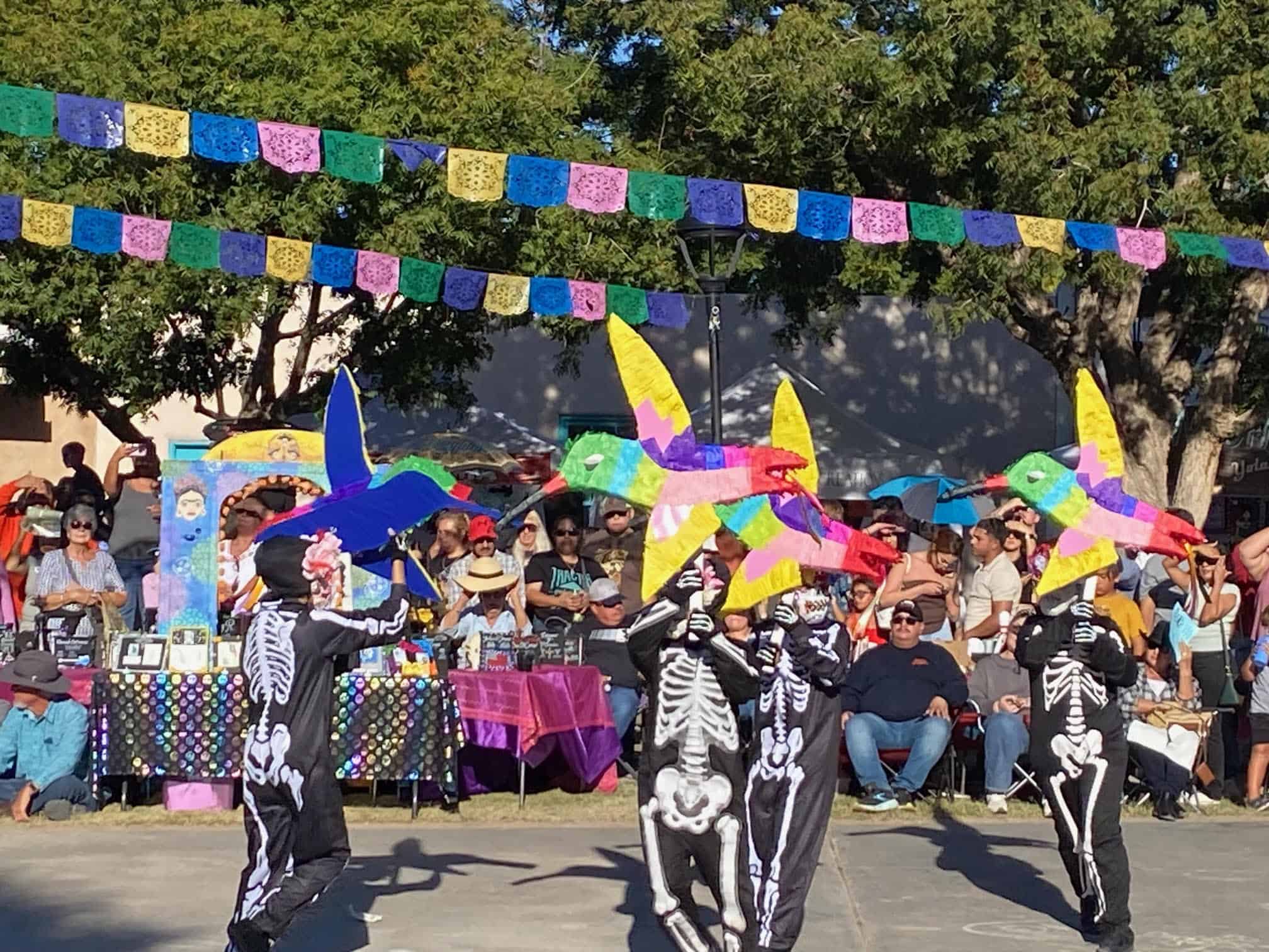 Dia de los Muertos celebration parade featuring performers dressed as skeletons dancing with colorful paper mache hummingbirds