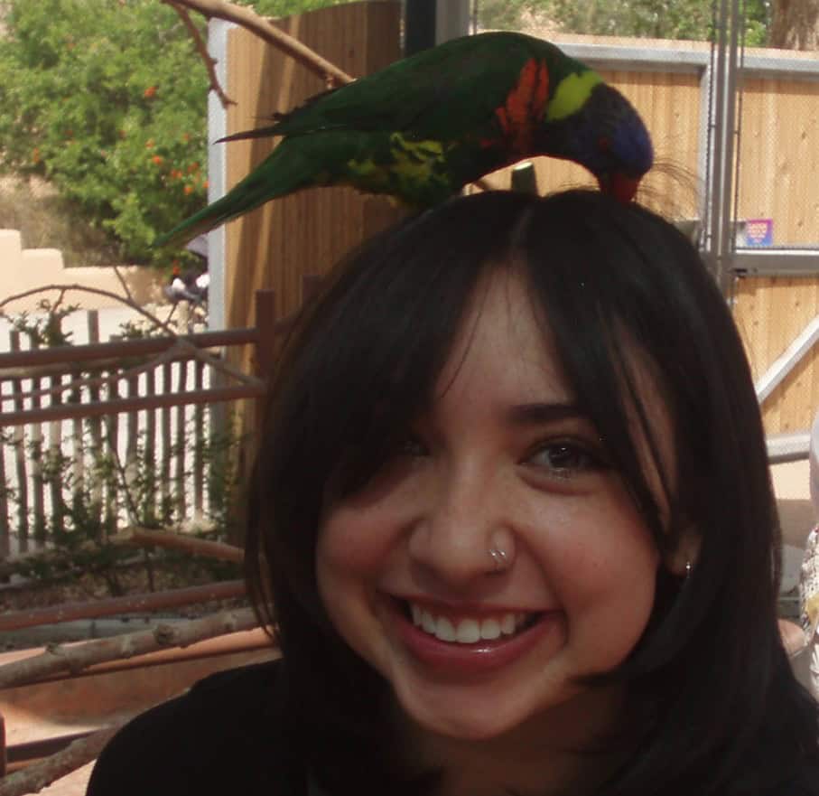 Brynn Mora smiling at the camera while a colorful parrot sits atop her head.