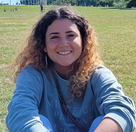 Photo of Coral Matos-Sepulveda sitting cross-legged in a field of grass