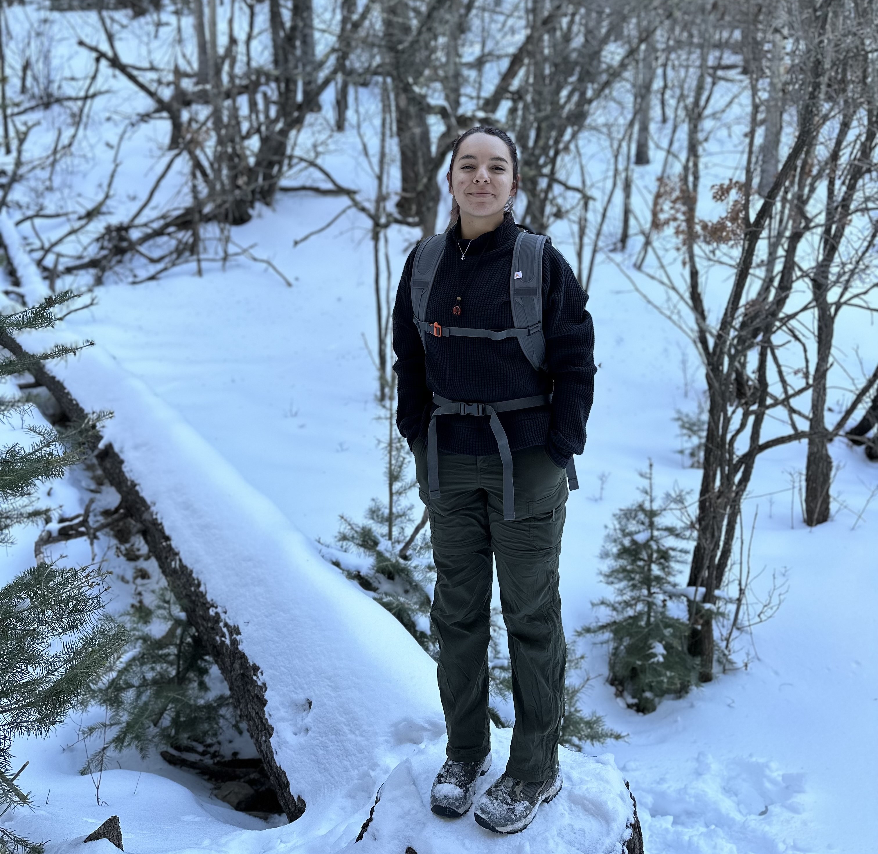 Emma Varel standing on a fallen, snow-covered tree surrounded by trees and snow.
